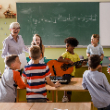  Elementary students in music class listening to a student playing the guitar